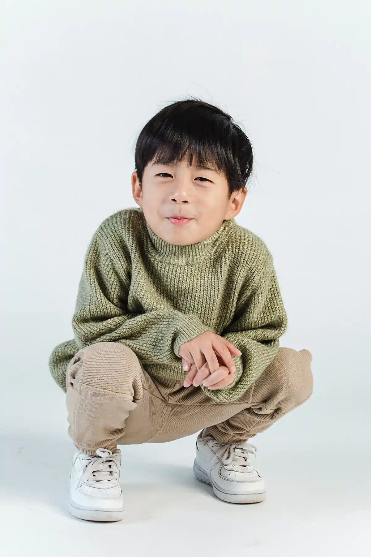 Young asian boy crouching and smiling during photoshoot.